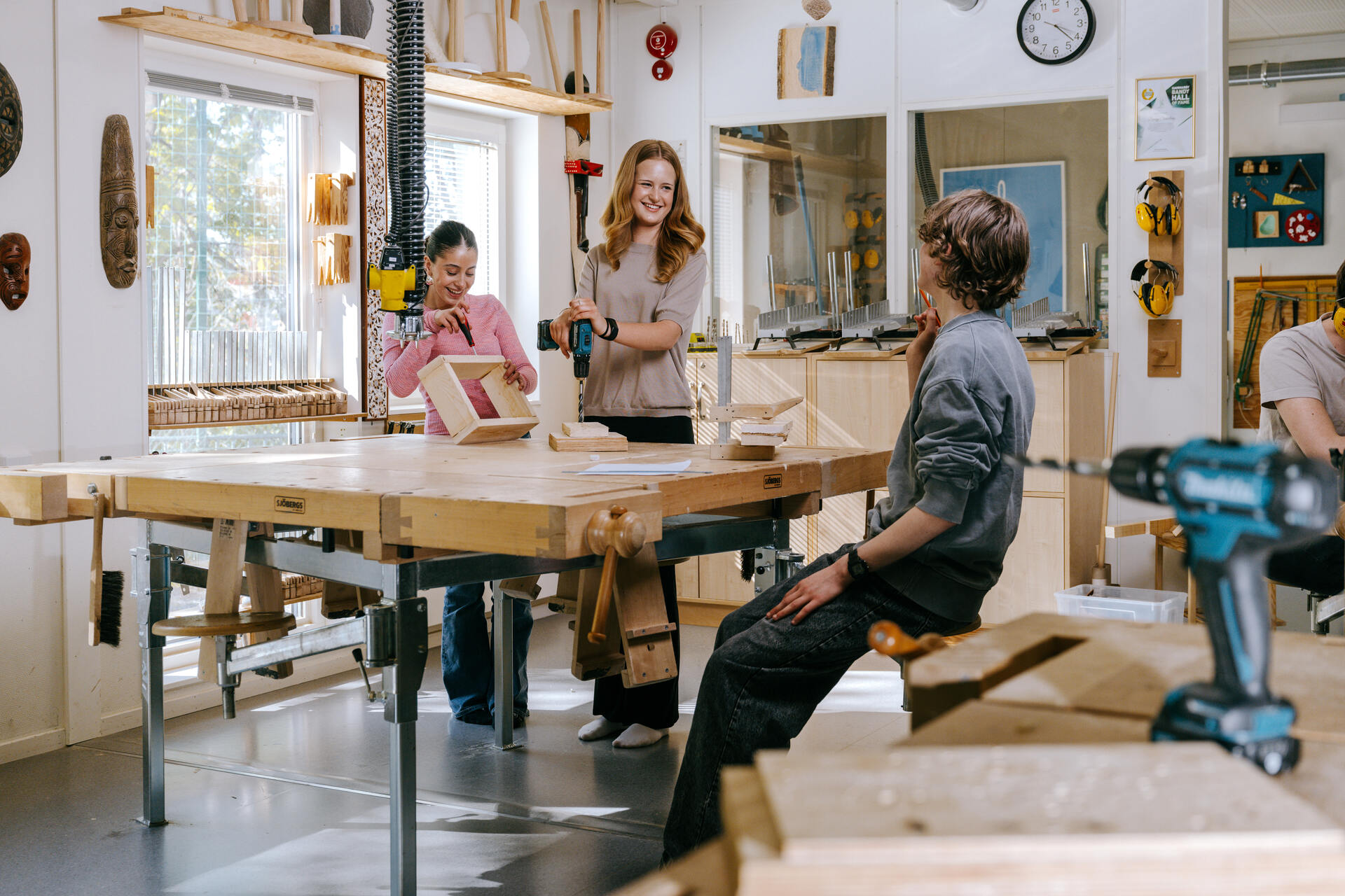 Elever arbeider sammen i en sløydsal på Ekens skole i Hammarby Sjöstad, hvor de borer og monterer tredeler rundt et arbeidsbord i et lyst og godt utstyrt undervisningsmiljø.
