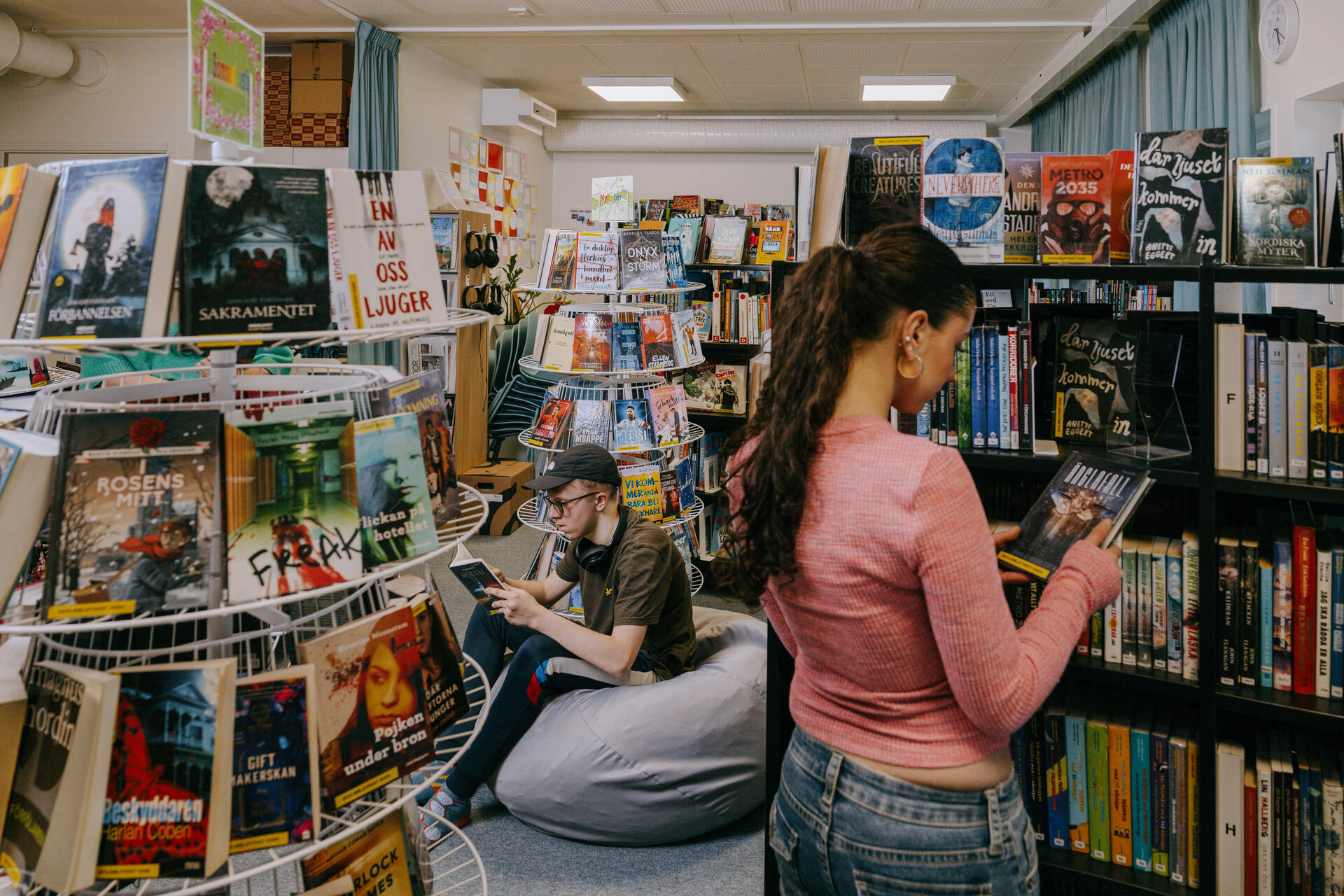 Elever oppholder seg i skolebiblioteket i Expandias modulløsning på Ekens skole i Hammarby Sjöstad, hvor de leser og velger bøker blant bokhyller i et rolig studiemiljø.