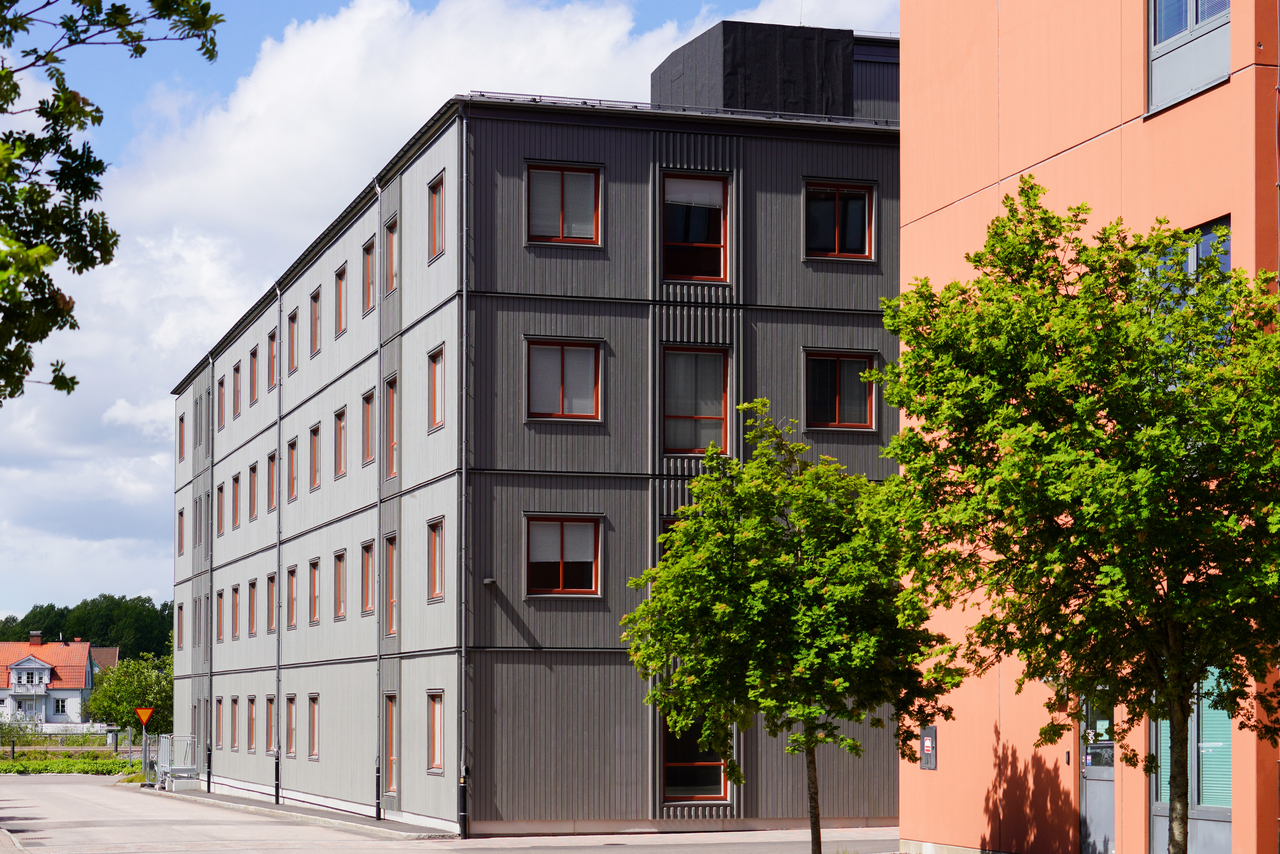 Eksteriørutsikt over kontormoduler fra Expandia ved Centralsjukhuset i Karlstad. Den fleretasje grå modulbygningen med store vinduer er plassert ved siden av sykehusets ordinære bygninger og omgitt av grøntområder, noe som viser hvordan Expandias kontormoduler smidig integreres i sykehusmiljøet for å skape moderne og fleksible arbeidsområder.