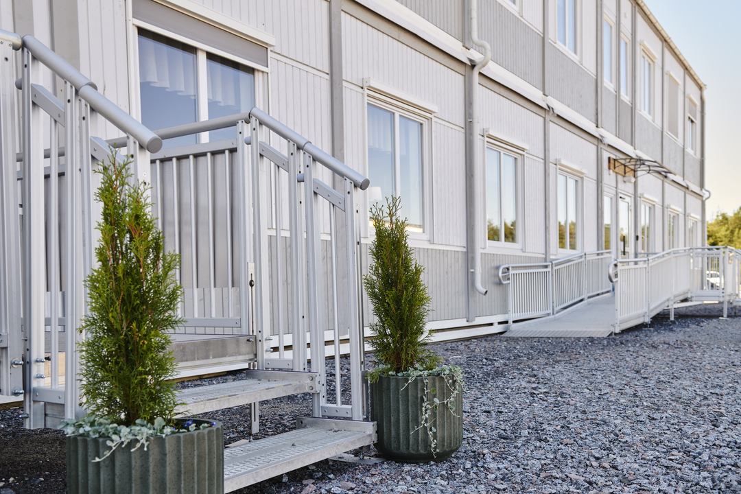 Eksteriør av kontormoduler fra Expandia med inngang, trapp og rampe med rekkverk. Fasaden er lys med flere vinduer, og gangarealer leder frem til inngangene. Bildet er tatt ved Alviks trafikk i Luleå.