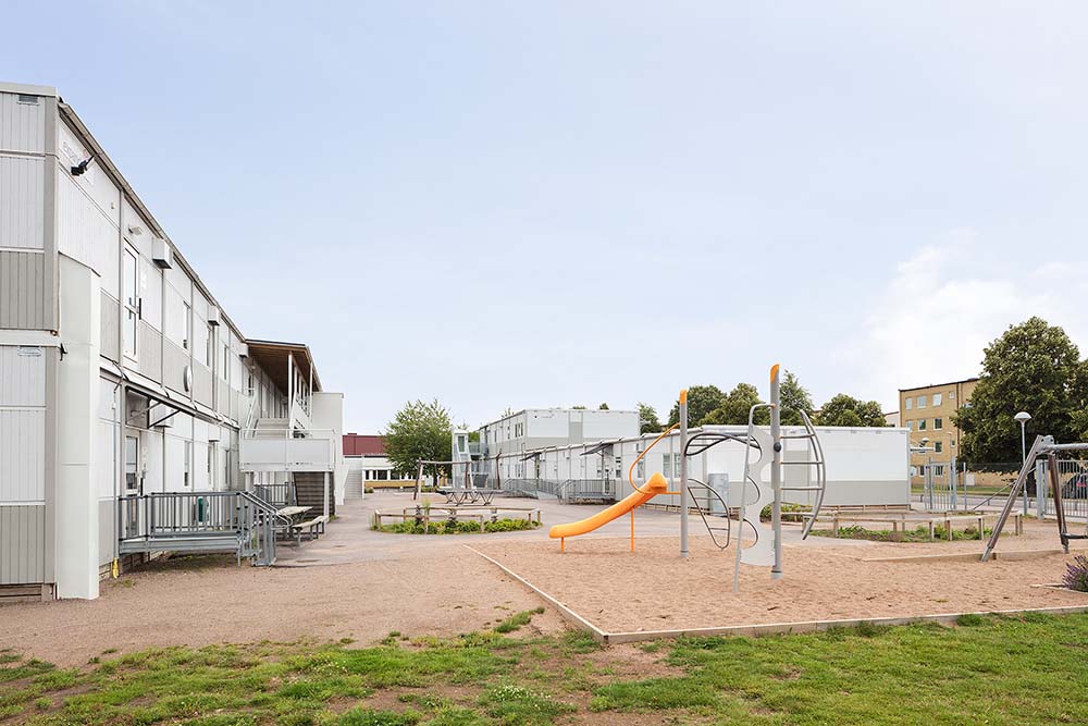 Skolmoduler från Expandia vid Rebbelberga skola i Ängelholm. Modulmiljö i två plan runt en skolgård med sandlåda, lekutrustning och öppna ytor för elever, utformad som en tillfällig skollösning.