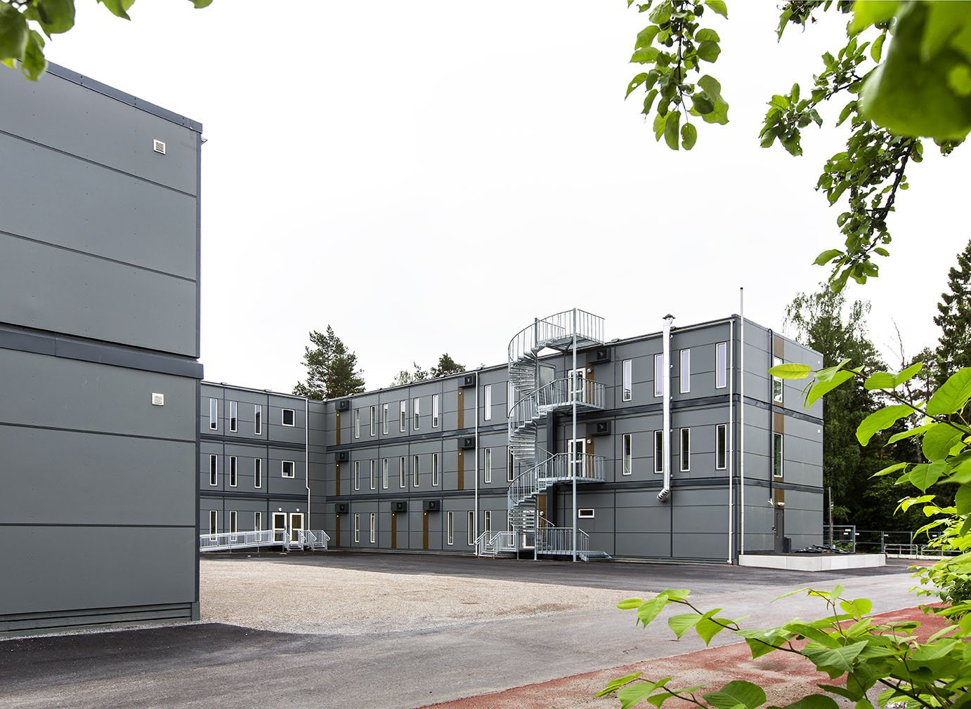 Falkbergsskolen i Tullinge med tre etasjer av sammenkoblede grå moduler, utvendig trappehus og store vinduer, plassert på en åpen skolegård – en fleksibel modulløsning fra Expandia.