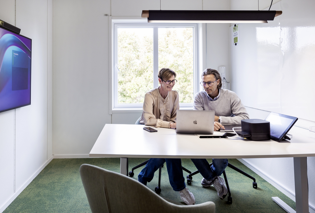 Møte- og arbeidsrom i kontormoduler hos Polypeptide, med ansatte som samarbeider ved bord og datamaskiner, utstyrt med skjermer, whiteboard, glassvegger, grønn teppebelagt gulv og moderne belysning i et lyst og funksjonelt kontormiljø – kontormoduler fra Expandia.