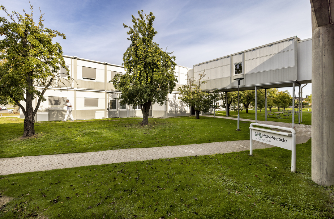 Kontormoduler hos Polypeptide plassert i grønt uteområde med gressplener, trær, gangveier og uteplasser med piknikbord, samt to-etasjes moduler med vindusrader – kontormoduler fra Expandia.