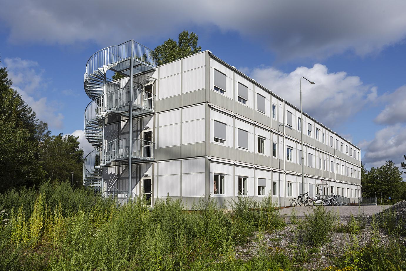 Midlertidig modulbygning fra Expandia i tre etasjer med kontorlokaler, plassert i grønt bymiljø, med lys fasade, mange vinduer og eksterne trapper.