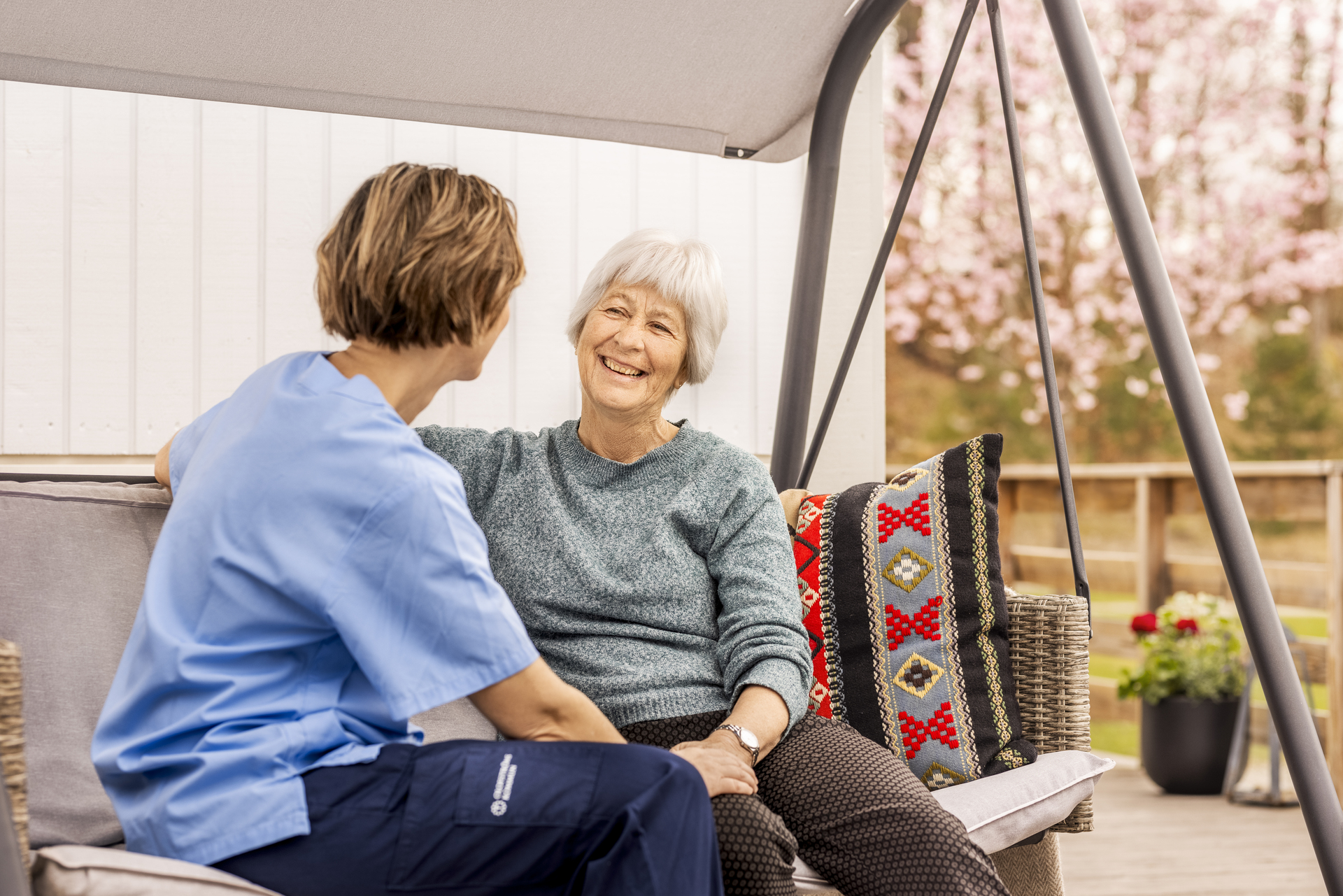 En beboer og omsorgspersonell sitter sammen utendørs ved Borggården demensomsorg i Olofström. De samtaler på en uteplass som inngår i en modulløsning fra Expandia.