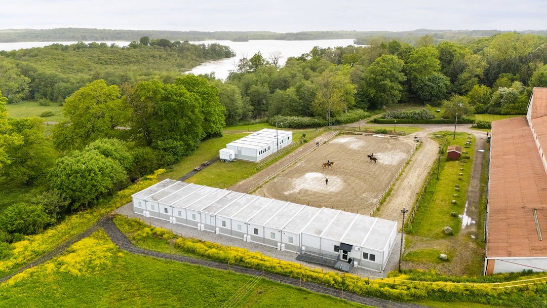 Drönarbild över Sveriges Ridgymnasium i Svedala med ridbana och omkringliggande grönområden. Intill skolområdet syns boendemoduler från Expandia som används som elevboenden, placerade i anslutning till verksamheten.