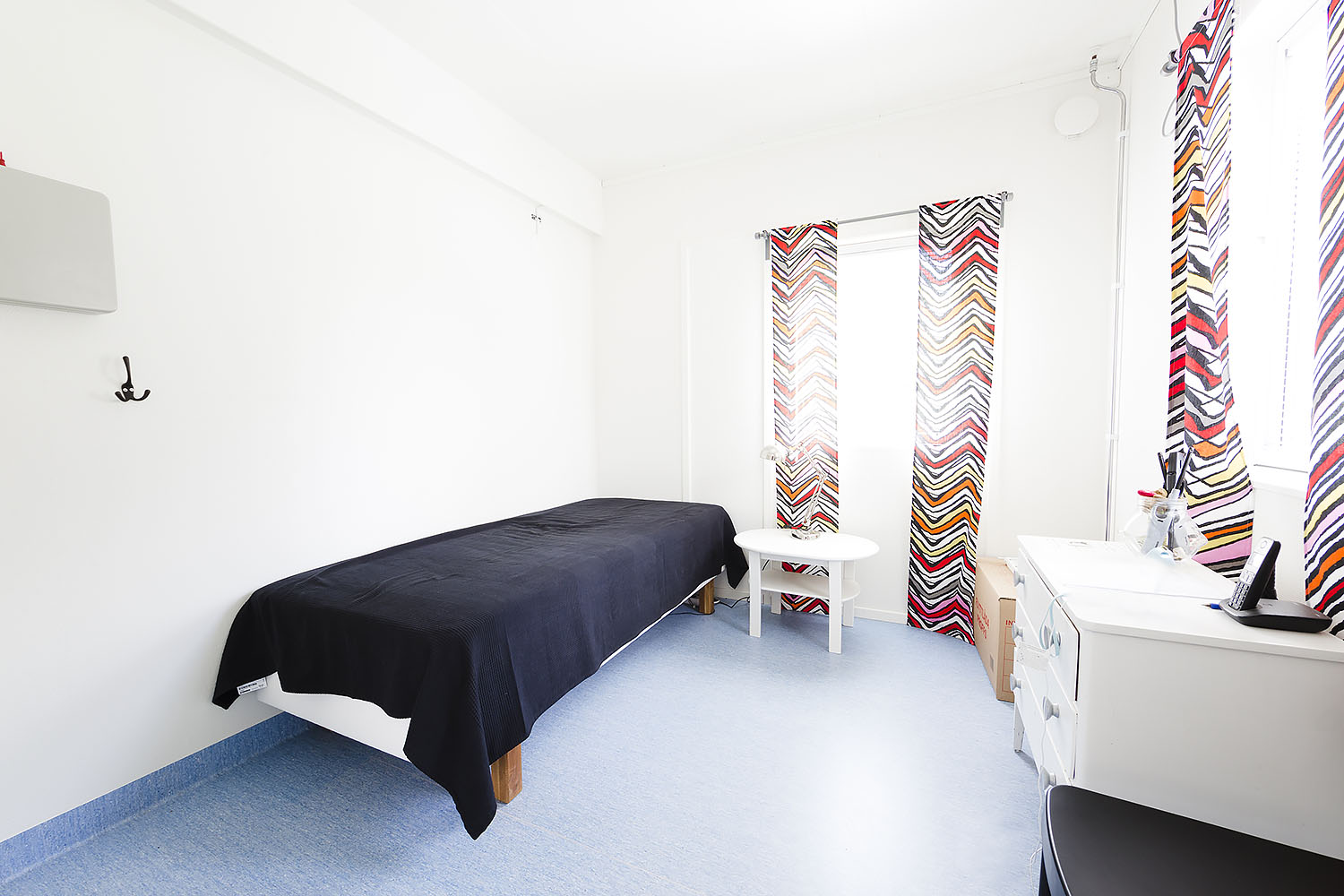 Ljust sovrum i boendemodul från Expandia med enkelsäng, litet bord, förvaring och fönster med mönstrade gardiner.