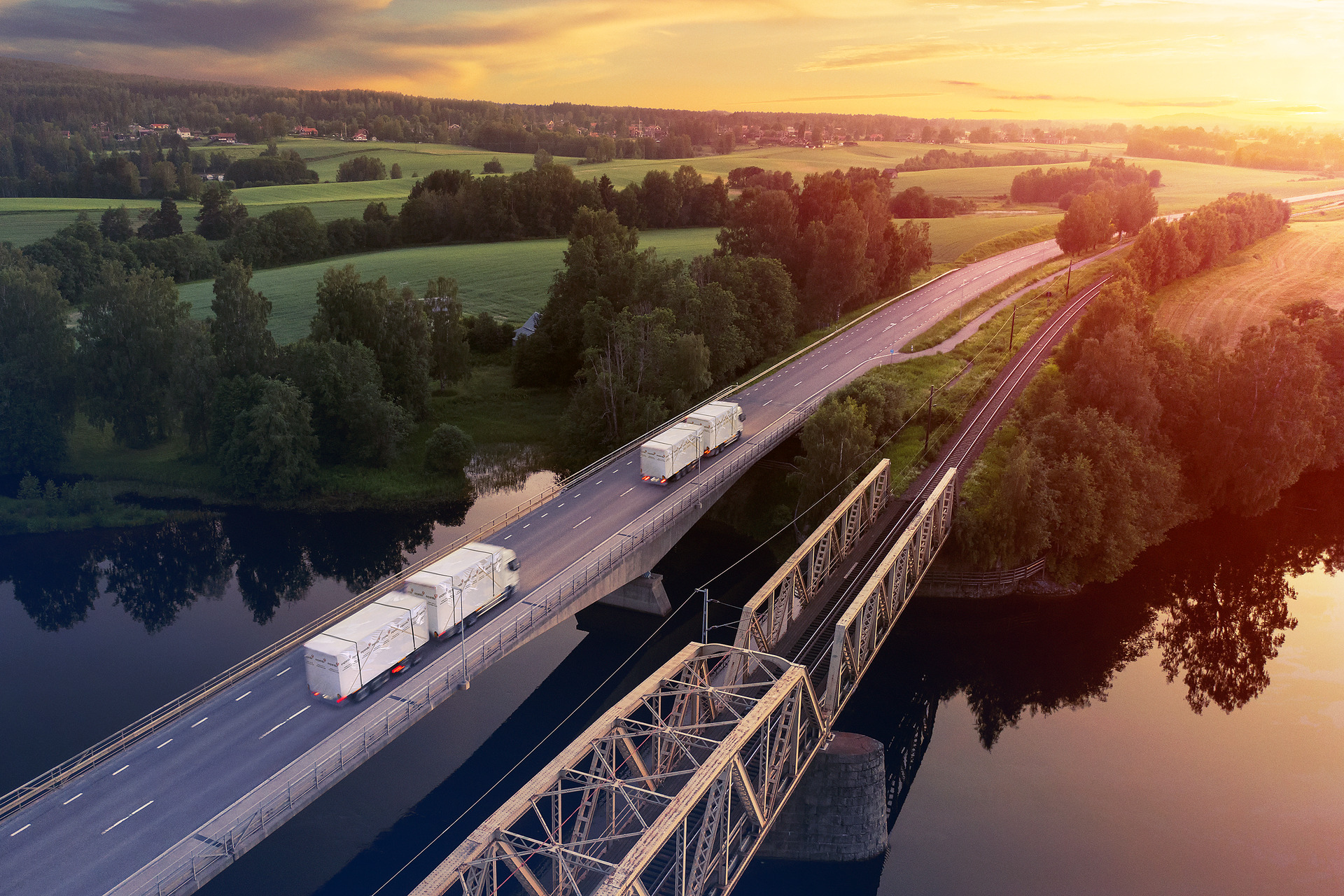 Lastebiler kjører i soloppgang ved siden av jernbane